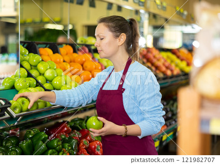 Middle-aged saleswoman putting apples on food stall in grocery store Middle-aged saleswoman putting apples on food stall in grocery store 121982707