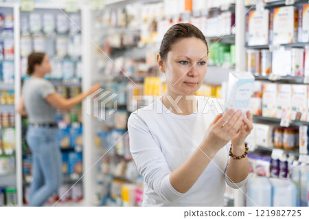 In pharmacy, woman carefully examines package of cream for problem skin In pharmacy, woman carefully examines package of cream for problem skin 121982725