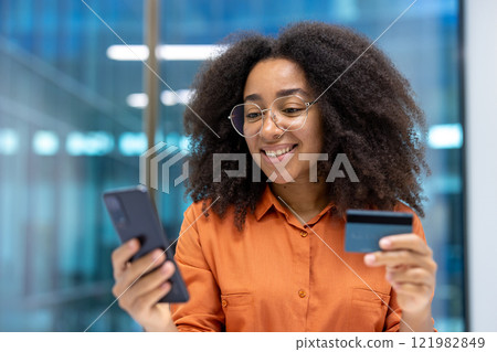 Young successful woman close-up at workplace inside office, businesswoman with phone and bank credit card, making purchases in online internet store, transferring funds using banking app. Young successful woman close-up at workplace inside office, businesswoman with phone and bank credit card, making purchases in online internet store, transferring funds using banking app. 121982849