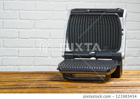 Black and silver electric grill on the wooden table near white brick wall 121983434