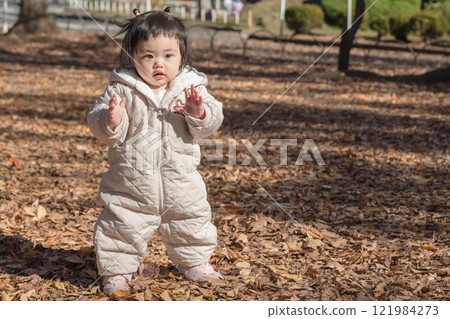 [一名 1 歲的孩子站在落葉覆蓋的冬季公園玩耍] 121984273