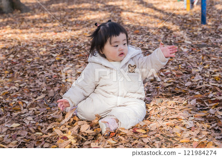[一名 1 歲的孩子坐在覆蓋著落葉的冬季公園裡玩耍] 121984274