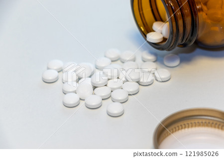 White pills spilling out of an overturned glass bottle 121985026