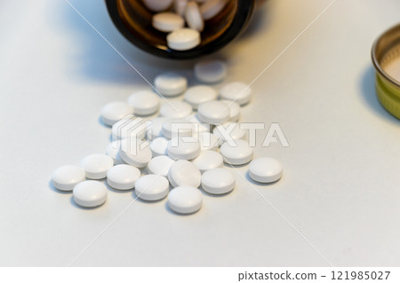 White pills spilling out of a fallen glass bottle 121985027