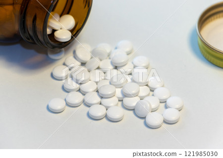 Many white pills spilled from a fallen bottle 121985030