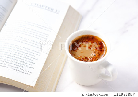 邊喝咖啡邊看書，打開一本平裝書（外國書），手裡拿著一個裝有咖啡的咖啡杯。 121985897