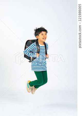 Elementary school boy jumping with a smile while carrying a school bag on his back Elementary school boy jumping with a smile while carrying a school bag on his back 121986005