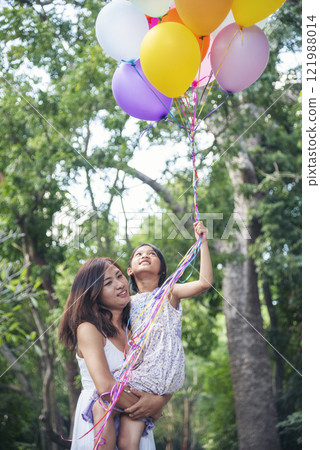 Vertical Happiness mother daughter play balloons together green garden park outdoor lifestyle. Happy family two people enjoy have fun cheerful. Mother childhood hand holding colorful balloons outside 121988014