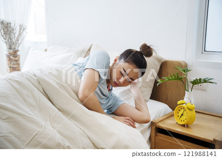 Asian women sleep wake up in white cozy bedroom happy time morning sunrise. Beautiful chinese use hand stop time alarm clock. Happy person lifestyle wake up in morning wellbeing relax sleepy napping 121988141