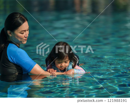 mother teaching toddler baby girl swimming in pool and wearing life jacket 121988191