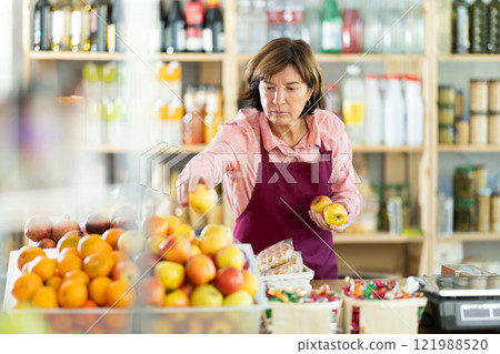Experienced female seller lays out ripe apples on store counter for sale Experienced female seller lays out ripe apples on store counter for sale 121988520