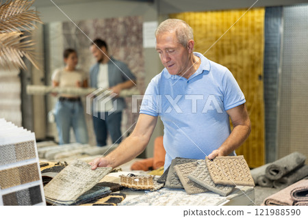 Elderly male shopper looks closely at carpet samples in hardware store Elderly male shopper looks closely at carpet samples in hardware store 121988590