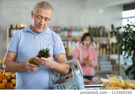 Grocery shopping at supermarket - man chooses olive oil while his wife chooses juice Grocery shopping at supermarket - man chooses olive oil while his wife chooses juice 121988598