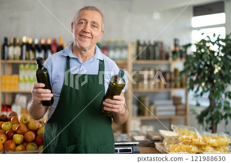 Senior man offers to buy vegetable oil, holds out bottles towards buyer, demonstrates best offers. 121988630