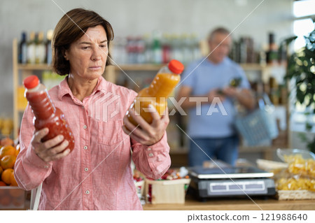 Elderly woman chooses peach and tomato juice 121988640