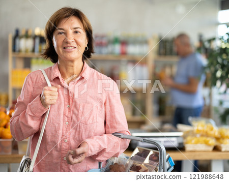 Visiting store, elderly woman is looking at something on shelf of showcase. Man buyer in background 121988648