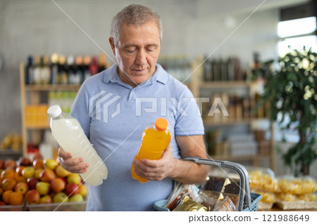 Mature man hold white plastic bottles and choose consider drink in store 121988649