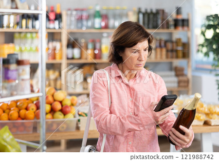 Mature woman is scanning QR on a bottle of beer in grocery 121988742