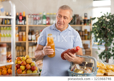 Mature man hold white plastic bottles and choose consider juice in store Mature man hold white plastic bottles and choose consider juice in store 121988746