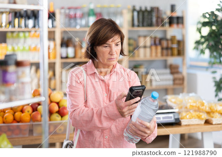 Mature woman is scanning QR on a bottle of water in grocery 121988790