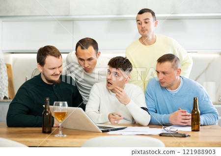 Group of friends watching football match on a laptop together and drinking beer Group of friends watching football match on a laptop together and drinking beer 121988903