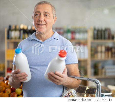 Mature man hold white plastic bottles and choose consider milk in store 121988915