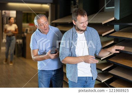 Mature man and guy son carefully examine wooden finishing material 121988925