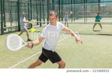 Active man engaged in padel in open-air court of tennis club Active man engaged in padel in open-air court of tennis club 121988932