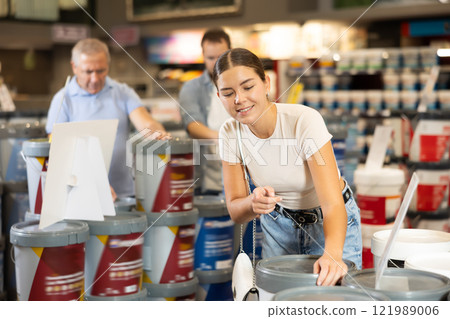 Woman buys jar with paint in paintwork material department of construction store for carrying out internal finishing work on object Woman buys jar with paint in paintwork material department of construction store for carrying out internal finishing work on object 121989006