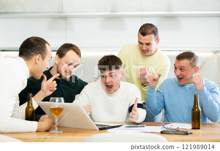 Group of friends watching football match on a laptop together and drinking beer Group of friends watching football match on a laptop together and drinking beer 121989014