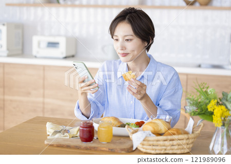 女人看著智能手機時吃早餐 女人看著智能手機時吃早餐 121989096