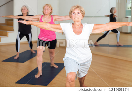 Group aged women standing in yoga pose indoors 121989174