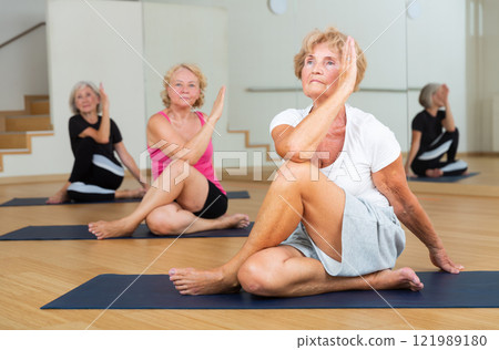 Elderly woman performing twisting asana Matsyendrasana during yoga class Elderly woman performing twisting asana Matsyendrasana during yoga class 121989180