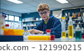 A young scientist is engaged in an exciting experiment in a colorful laboratory. The environment is bright, filled with various glassware and chemicals. Curiosity and discovery are at the heart of 121990215