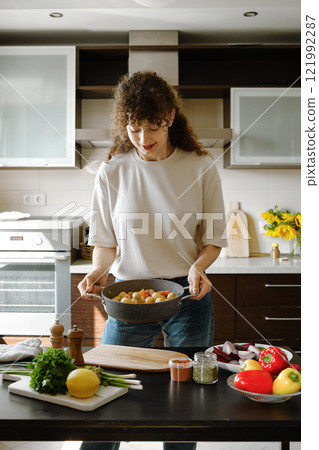 Woman lifting a baking pan with vegetables standing near the kitchen table Woman lifting a baking pan with vegetables standing near the kitchen table 121992287