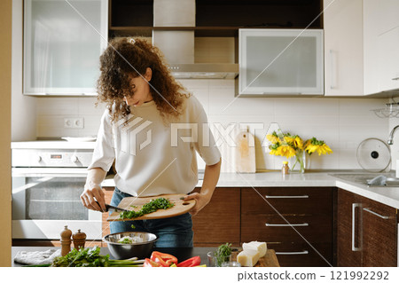 Woman pouring cilantro from cutting board into a bowl with stuffing Woman pouring cilantro from cutting board into a bowl with stuffing 121992292