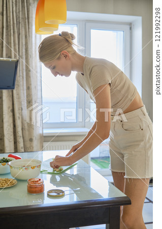 Young woman preparing healthy food in a bright kitchen during the day Young woman preparing healthy food in a bright kitchen during the day 121992298