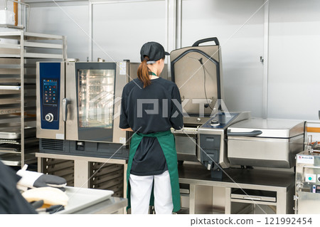 A female chef using a fryer in the kitchen A female chef using a fryer in the kitchen 121992454
