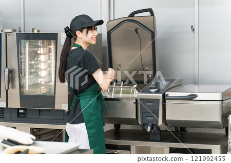 A female chef using a fryer in the kitchen A female chef using a fryer in the kitchen 121992455