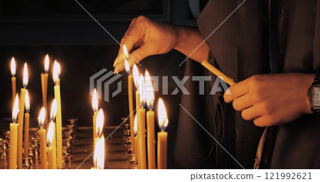 Traditional act of lighting candles during religious rituals, symbolizing hope, faith, and spiritual devotion. Soft flames create peaceful atmosphere in sacred church ceremony. Christianity concept 121992621