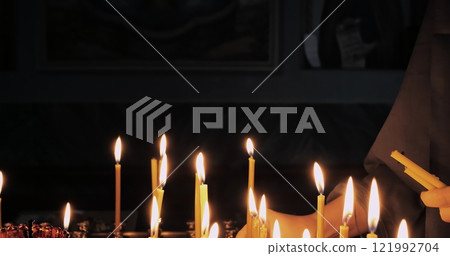 Faithful woman ignites candles in holy church, expressing devotion and connection with god. Traditional orthodox ritual amidst glowing candlelight in a tranquil and spiritual setting. 121992704