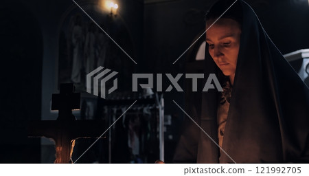 Woman praying near lit candles in church, immersed in peaceful devotion. Warm glow of flames enhancing spiritual atmosphere, connecting faith with sacred traditions of prayer. Christianity concept 121992705