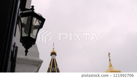 Orthodox church steeples captured through the perspective of an old lantern against a cloudy sky, merging tradition with a serene and reflective ambiance. A spiritual and cultural landmark. Orthodox church steeples captured through the perspective of an old lantern against a cloudy sky, merging tradition with a serene and reflective ambiance. A spiritual and cultural landmark. 121992706