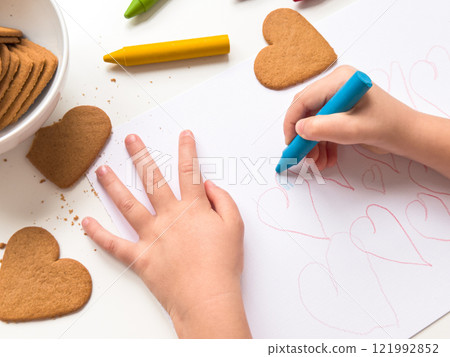 Child drawing hearts with crayons near heart shaped cookies on a table Child drawing hearts with crayons near heart shaped cookies on a table 121992852
