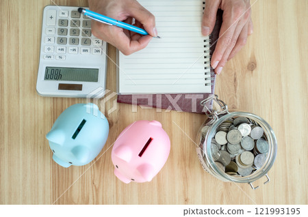 Cropped shot view of someone try to counting saving money by calculator and write it on book. Cropped shot view of someone try to counting saving money by calculator and write it on book. 121993195