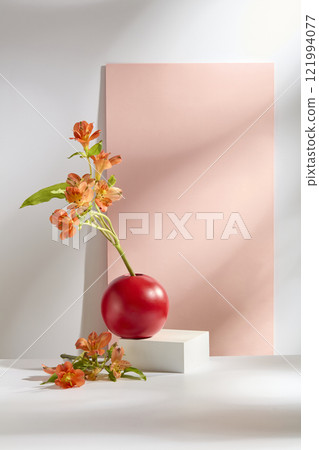 Frontal view of an empty white cube podium as a product platform, decorated with a red vase of orange alstroemeria flowers. The New Year concept is set against a white backdrop featuring a pink panel. 121994077