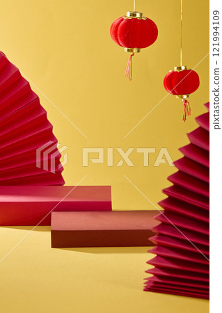 A minimalist product display for the Lunar New Year theme. Frontal view of two empty crimson podiums, decorated with red paper fans arranged against a yellow background with hanging red lanterns. 121994109