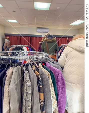 Thrift store shoppers browse racks of clothing. High quality photo 121994167