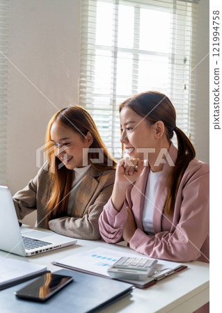 Businesswoman sitting at desk on couch in workplace or at home working on laptop and analyzing data on charts and graphs and writing on papers to make business plan and strategies for company 121994758