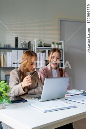 Businesswoman sitting at desk on couch in workplace or at home working on laptop and analyzing data on charts and graphs and writing on papers to make business plan and strategies for company 121994759